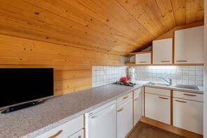 Een keuken met houten plafond, witte kasten, een granieten aanrechtblad en een inbouwfornuis.