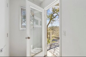 Eine weiße Tür, die auf einen Balkon mit Blick auf Bäume und einen Zaun führt.