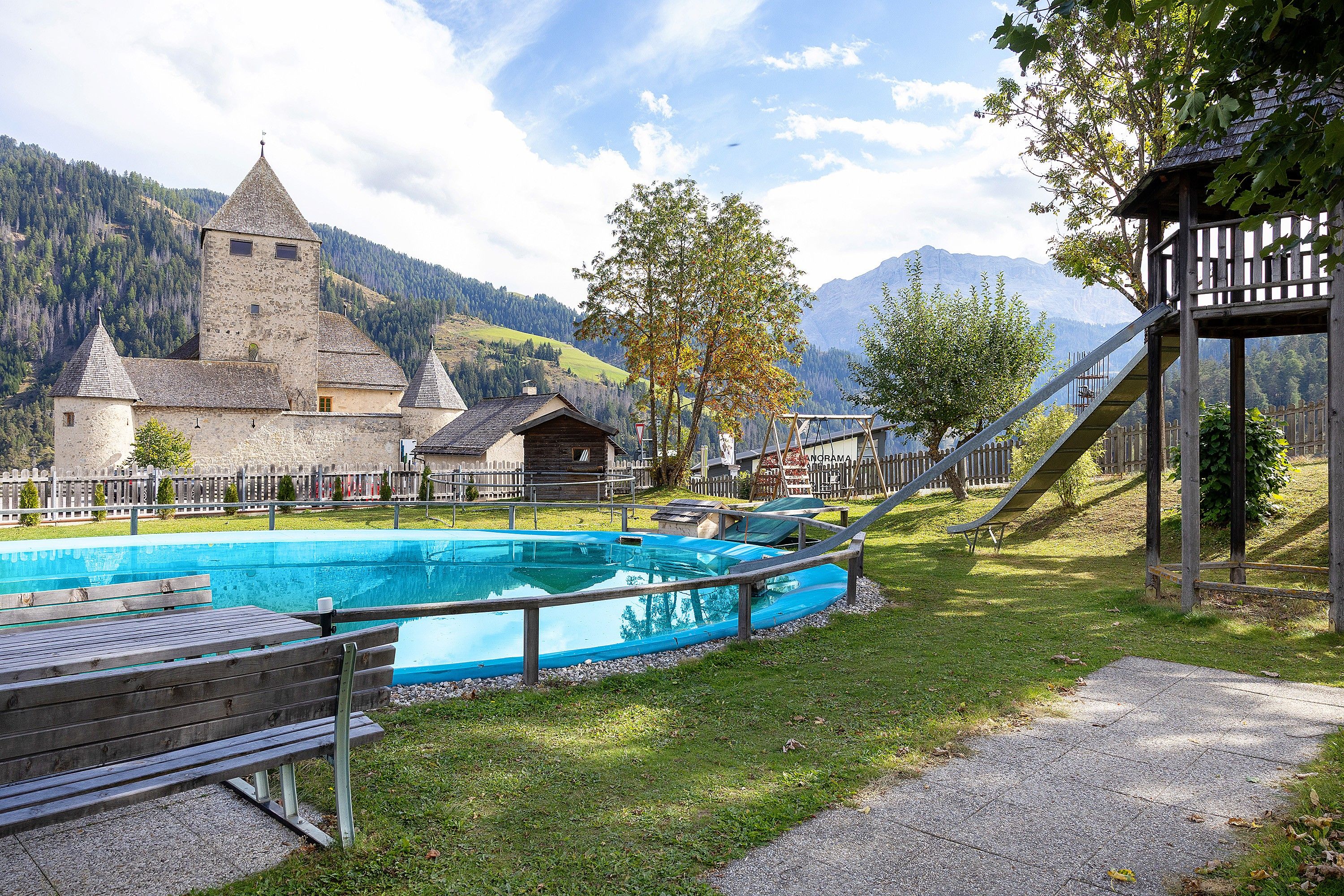 Une piscine dotée d’une terrasse en bois et de bancs, entourée d’une clôture en bois et d’arbres.
