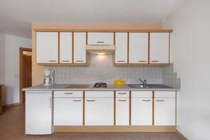 Una cocina compacta con armarios blancos, estufa integrada y cafetera.