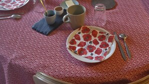 Une table à manger recouverte d’une nappe à motifs, avec différents plats, des tasses et un téléviseur en arrière-plan.