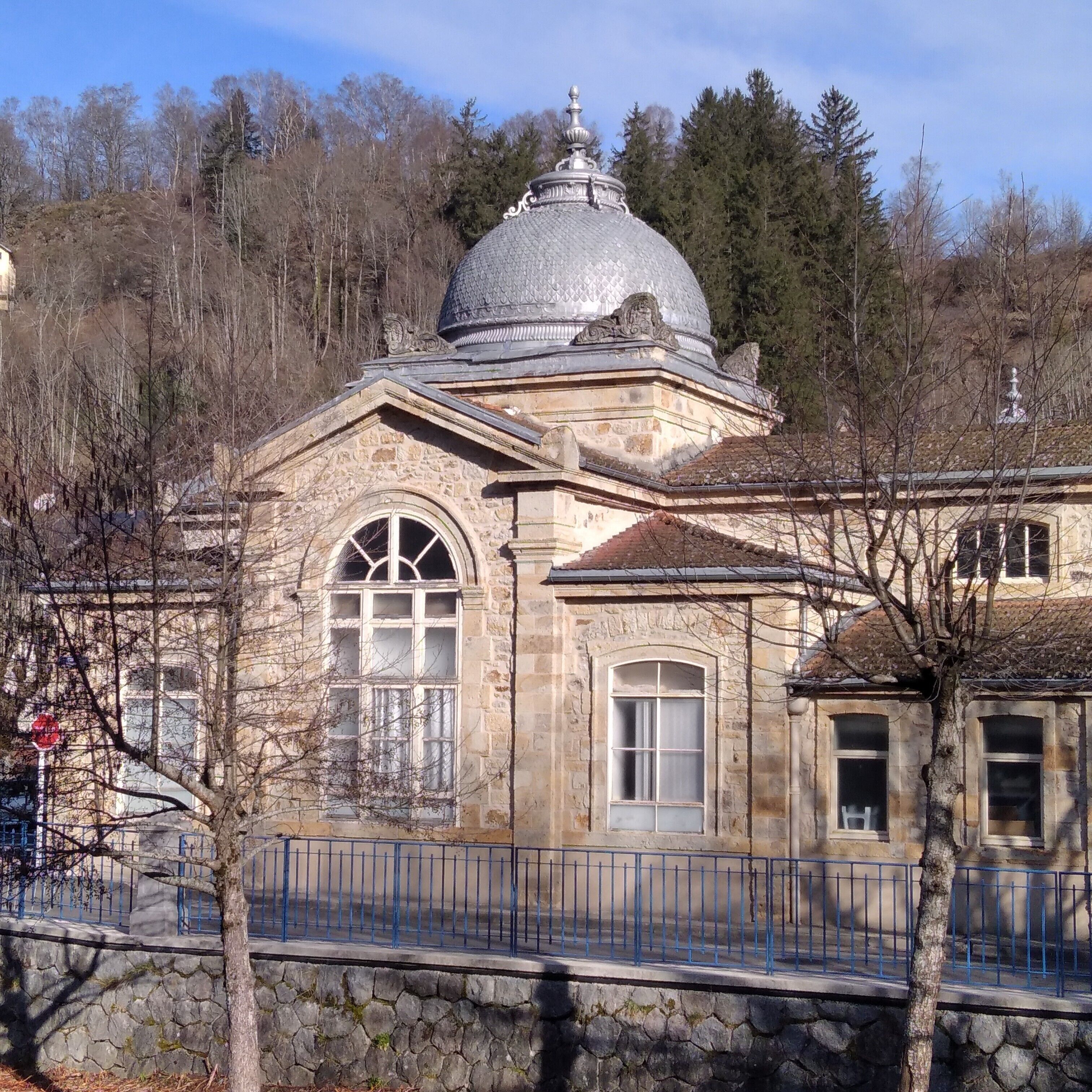 A stone building with a dome, arched windows, and a stone fence.