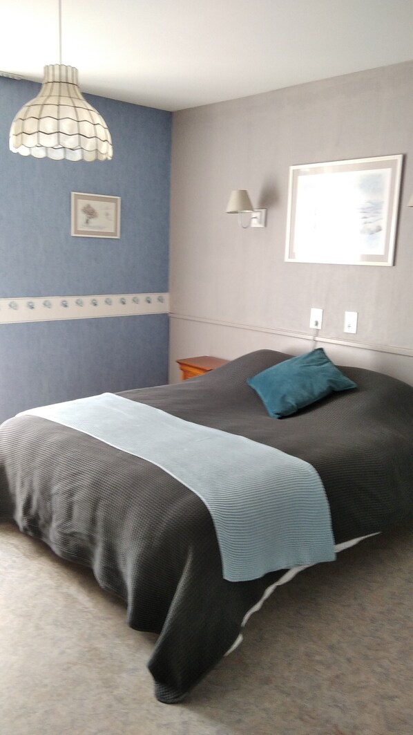 Ein Schlafzimmer mit einem Bett, einer Wandlampe, einem gerahmten Bild und einer dekorativen Wandverkleidung.