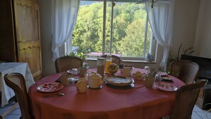 A dining table set with various dishes and drinks, surrounded by wicker chairs, with a view of trees through a window. - Apartment in A Hotel 'Villa Des Fleurs Ch Hélène N°27' with Mountain View and Wi-Fi (La Bourboule)