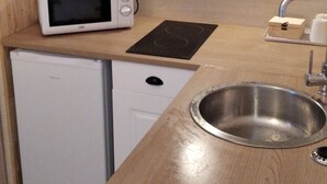 Une cuisine compacte équipée d’un four à micro-ondes, d’un petit réfrigérateur, d’un évier et de carreaux décoratifs sur le mur derrière l’évier.
