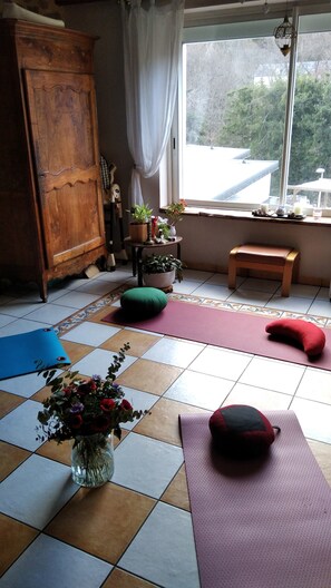 A room with a wooden cabinet, a window with a view, a small table with plants, and exercise mats on the floor. - Apartment in A Hotel 'Villa Des Fleurs Ch Hélène N°27' with Mountain View and Wi-Fi (La Bourboule)