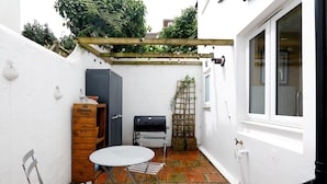 Eine kleine Terrasse mit Tisch und Stühlen, einem Grill und einer Holzkiste mit der Aufschrift 'Corona Extra'.