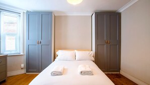 Ein Schlafzimmer mit einem Bett, zwei grauen Kleiderschränken, einem Nachttisch und einem Fenster mit Jalousien.