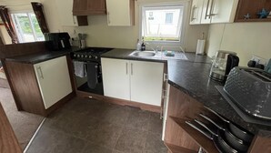 A compact kitchen with a stove, sink, and countertop appliances. - Cabin Sleeps 6 With Garden and Pets Welcome (Cowes)