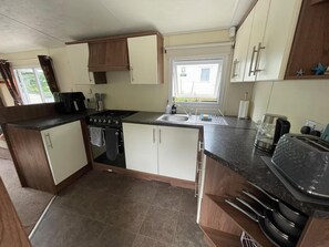 A compact kitchen with a stove, sink, and countertop appliances. - Cabin Sleeps 6 With Garden and Pets Welcome (Cowes)