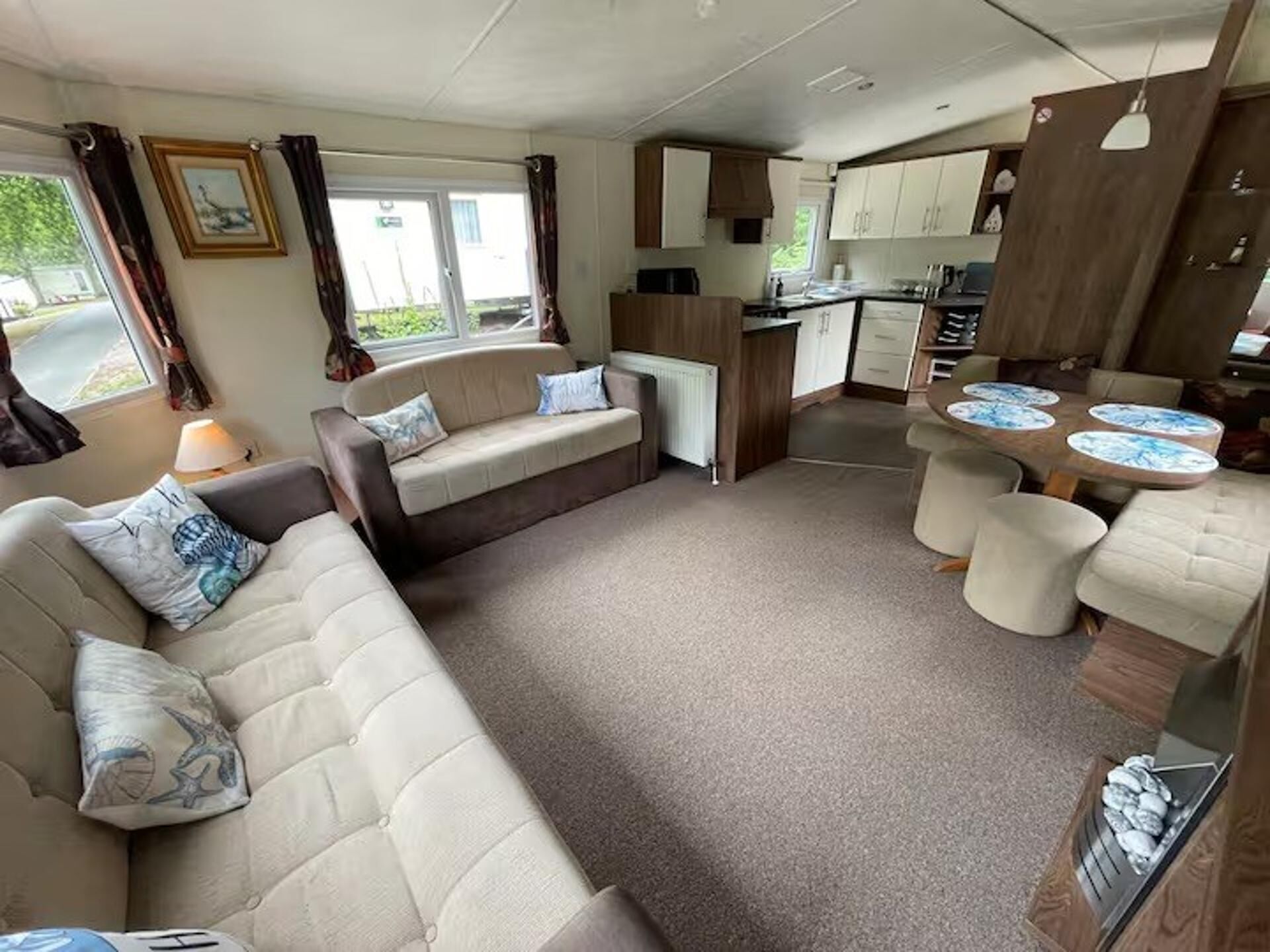 Interior compacto de una caravana con sofá, mesa de comedor y sillas, kitchenette y ventana.