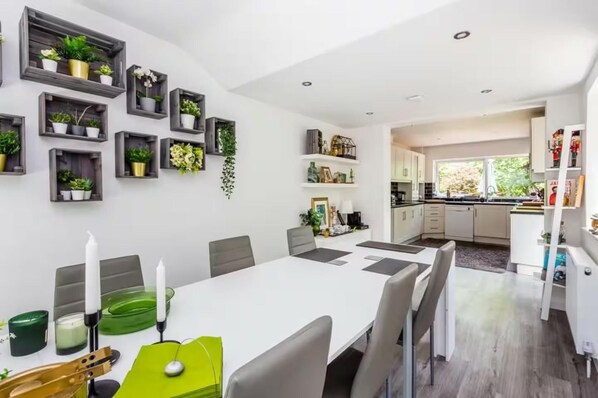 A modern kitchen with white cabinets, a dining area with a white table and chairs, and a kitchen island.