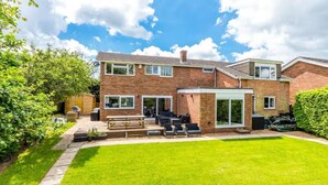 A two-story brick house with a patio, outdoor seating, and a well-maintained lawn.