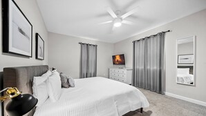 Ein Schlafzimmer mit einem Bett, einem Deckenventilator, einem Fernseher und einer Kommode.