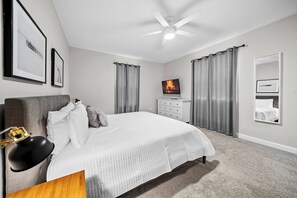 Ein Schlafzimmer mit einem Bett, einem Deckenventilator, einem Fernseher und einer Kommode.