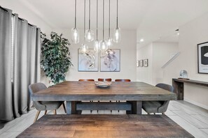A dining area with a wooden table, chairs, hanging pendant lights, and a plant. - 5BR house with game room near Disney area (Kissimmee)