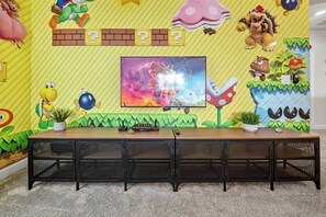 Ein Mario-Themenzimmer mit einem langen Tisch, einem Fernseher und verschiedenen Dekorationen.
