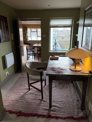 Ein Zimmer mit Tisch, Stuhl, Lampe, Fenster mit Aussicht und einem gemusterten Teppich.
