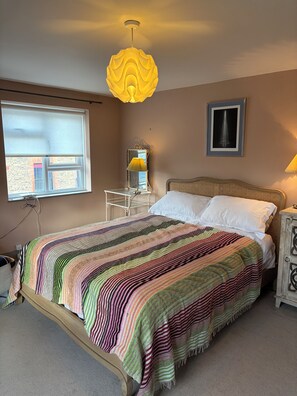 Ein Schlafzimmer mit einem Bett, einem Nachttisch, einer Lampe, einem Fenster und einem Wandbild.
