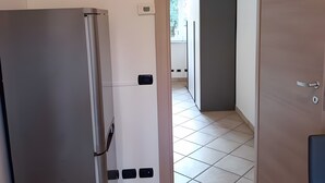 Una cocina con refrigerador, puerta que da a un balcón y piso de baldosas.