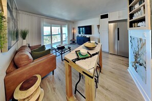 A modern kitchen with a dining area, a sofa, and a TV. - Casa Del Mar 313 | Great Pool + Beach Views (Galveston)