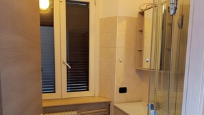 Een badkamer met raam, radiator, wastafel en een douchecabine van glas.