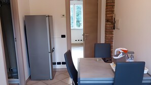 Een kleine keuken met een koelkast, een eettafel met stoelen en uitzicht door een open deur op een balkon.