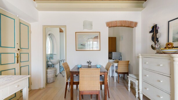 Un comedor con una mesa de madera, sillas de mimbre y un aparador blanco.