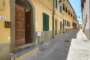 Una estrecha calle adoquinada con edificios amarillos, puertas de madera y contraventanas verdes.