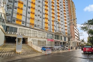 Ein mehrstöckiges Gebäude mit einem Geschäft im Erdgeschoss, einer Treppe, die zu einem Eingang führt, und geparkten Fahrzeugen vor der Straße.