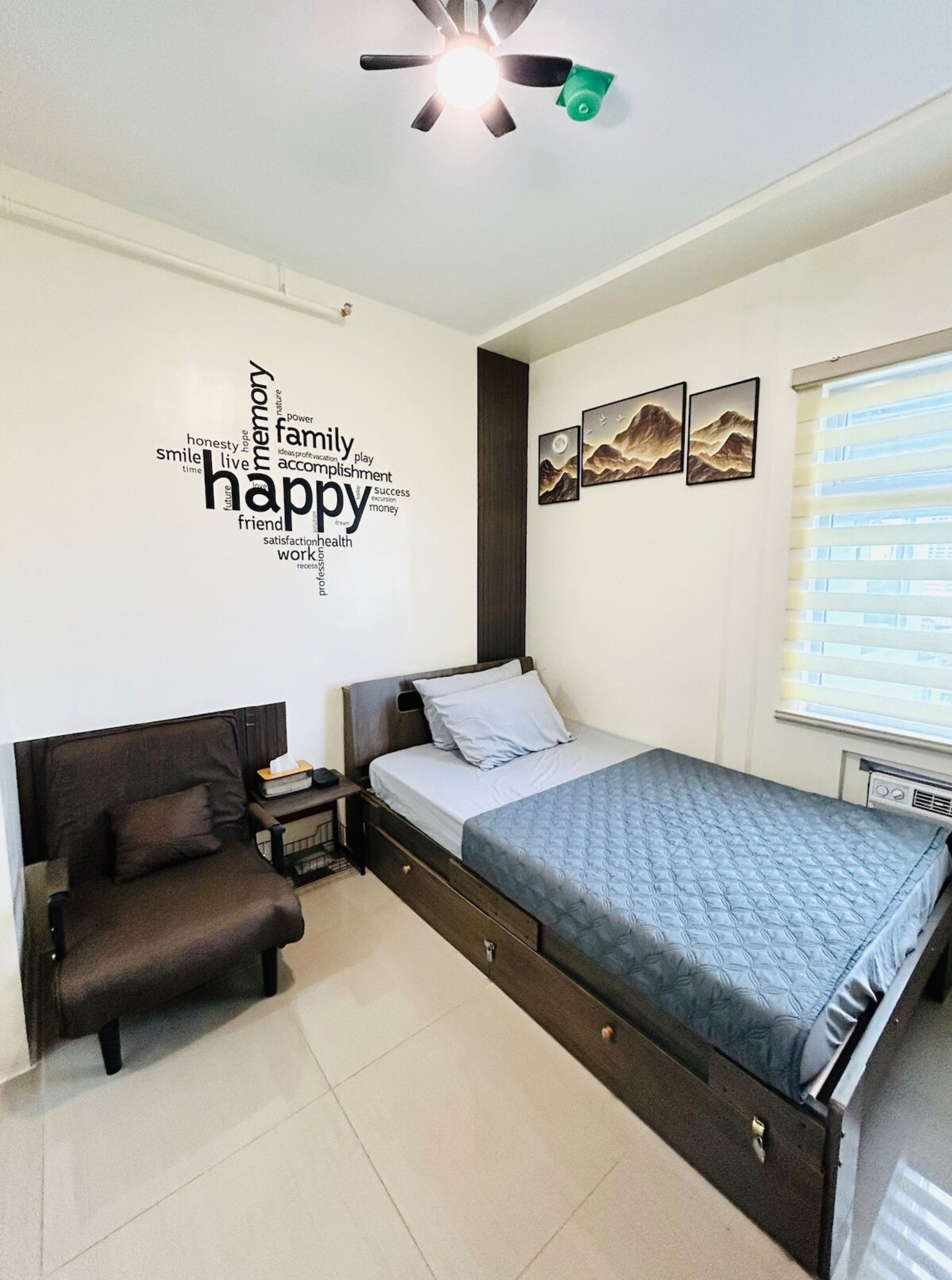 A bedroom with a bed, a chair, a nightstand, a ceiling fan, and wall art.
