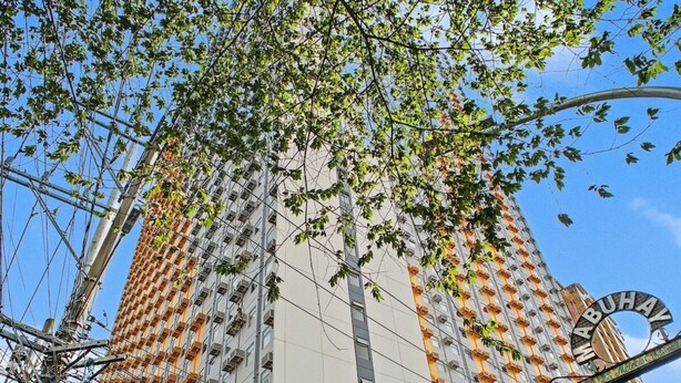 Un immeuble de grande hauteur à la façade distinctive, aux couleurs orange et blanche, doté de nombreux balcons, et se dressant sous un ciel dégagé.