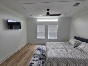 A bedroom with a bed, a ceiling fan, a mounted TV, and two windows with blinds. - Pleasant 3-bedroom house with AC in vibrant Houston (Houston)