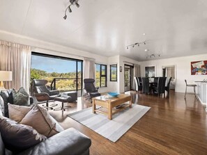 A spacious living room with a large window, a dining area, and a kitchen. - Charlie Bravo Chalet—Escape to the Golden Triangle (Margaret River)