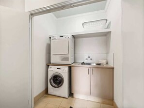 A laundry room with a washing machine, dryer, and a small countertop with a sink and towel rack. - Charlie Bravo Chalet—Escape to the Golden Triangle (Margaret River)