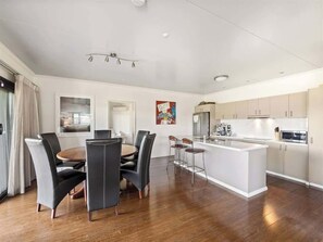 A modern kitchen with a central island, a dining area with a round table and chairs, and a view of the city through large windows. - Charlie Bravo Chalet—Escape to the Golden Triangle (Margaret River)
