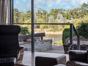 A deck with outdoor seating, a stone wall, and a view of a lake and forest. - Charlie Bravo Chalet—Escape to the Golden Triangle (Margaret River)