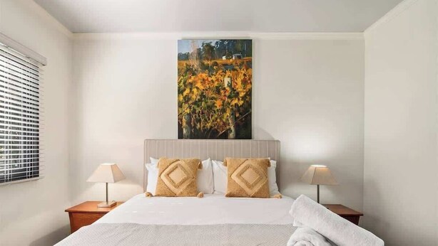 A hotel room with a large bed, two bedside lamps, a painting above the bed, and a window with blinds. - Charlie Bravo Chalet—Escape to the Golden Triangle (Margaret River)