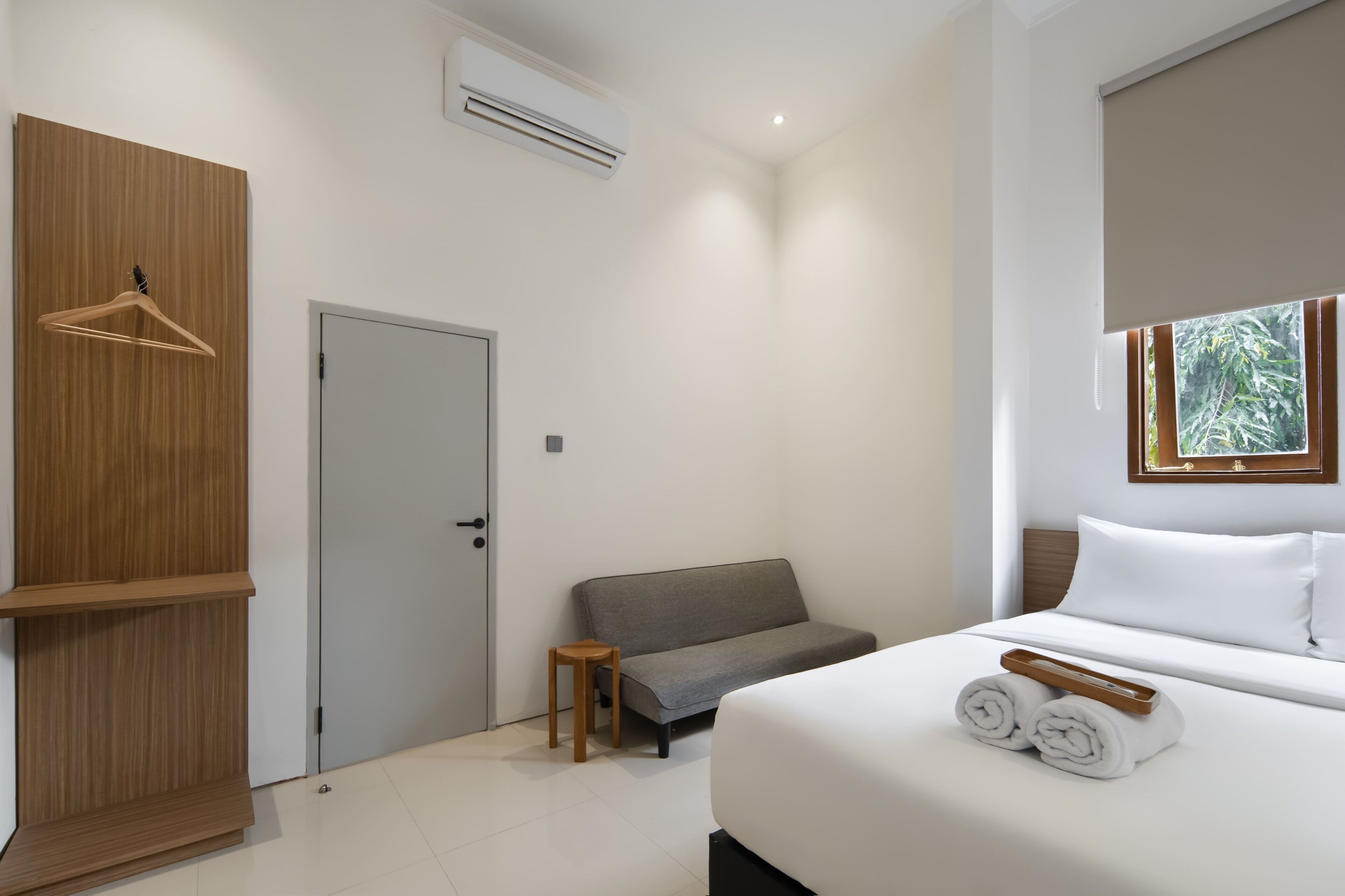 Een moderne hotelkamer met een bed, een grijze bank, een houten garderobe en een klein houten krukje.