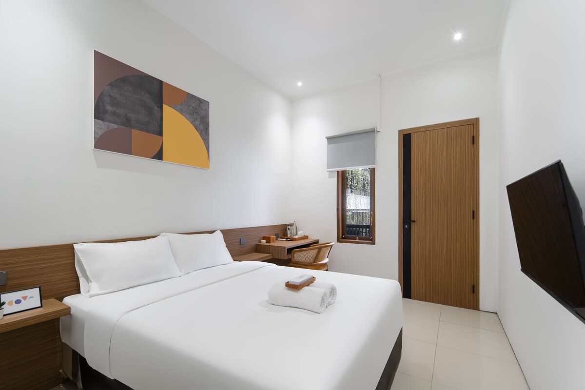 A hotel room with a bed, a desk, a chair, a TV, and a window.