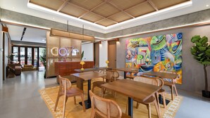 Un interior moderno con mesas y sillas de madera, un cuadro abstracto colorido y un mostrador de recepción.