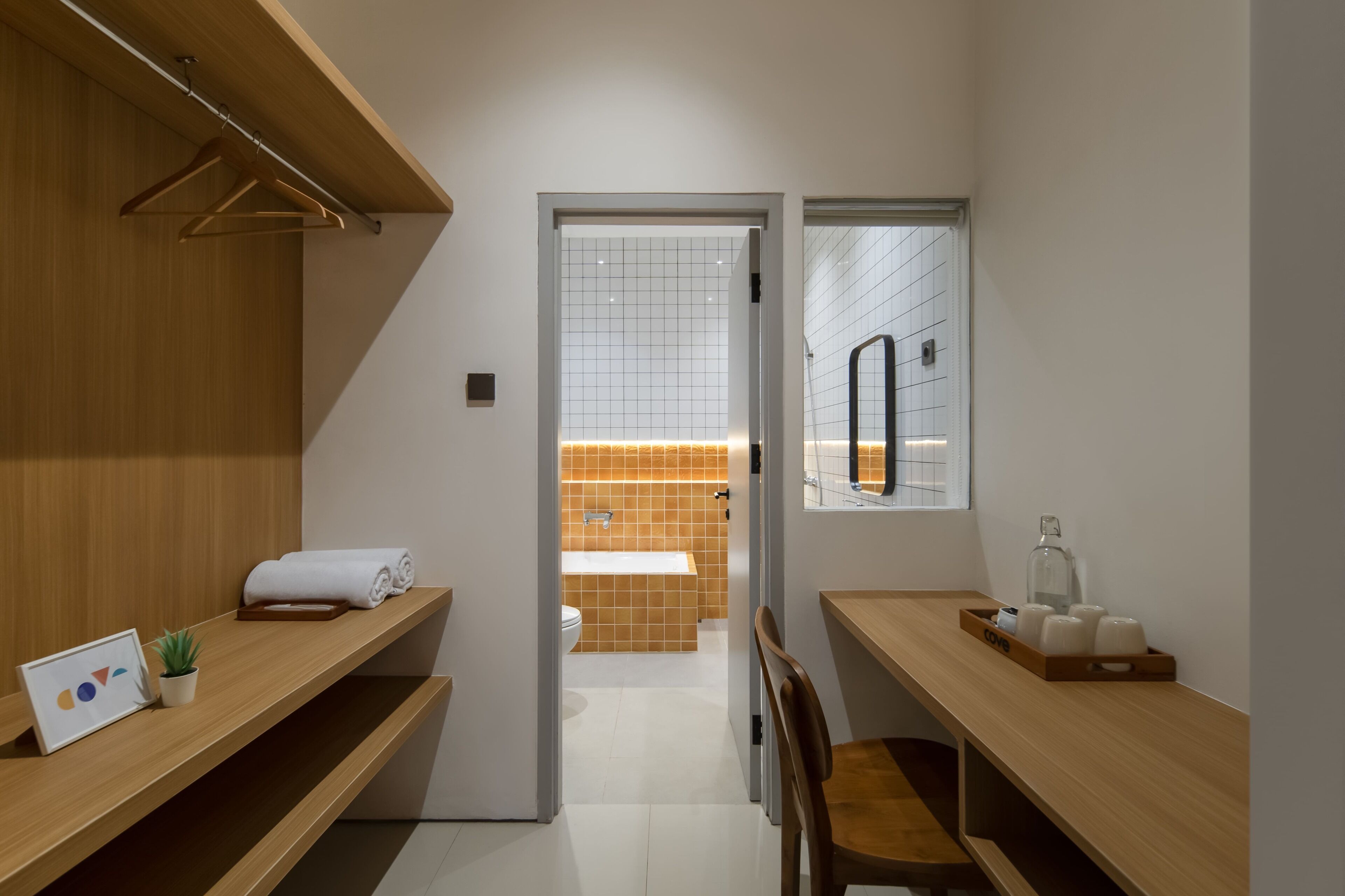 Un baño moderno con ducha, inodoro y lavamanos. Hay estantes de madera con toallas y una planta pequeña.
