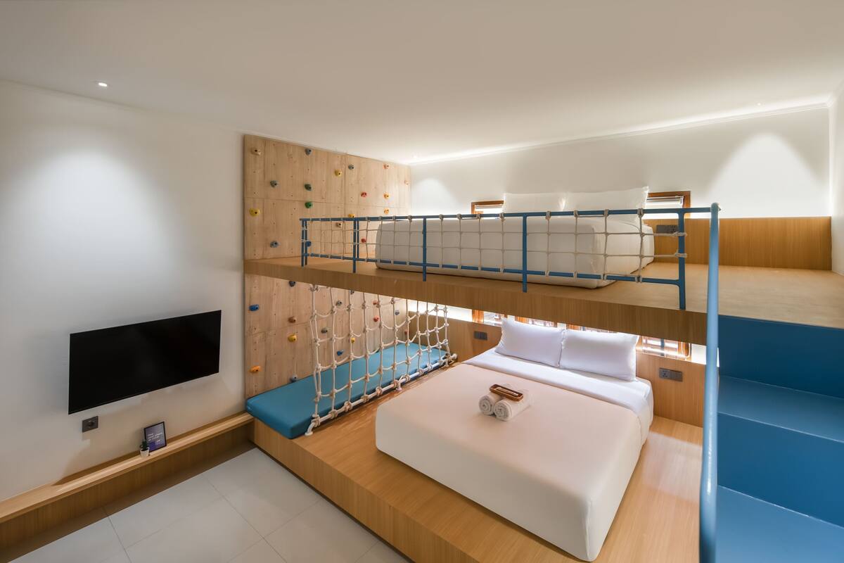 A bunk bed room with a climbing wall, a flat-screen TV, and a wooden floor.