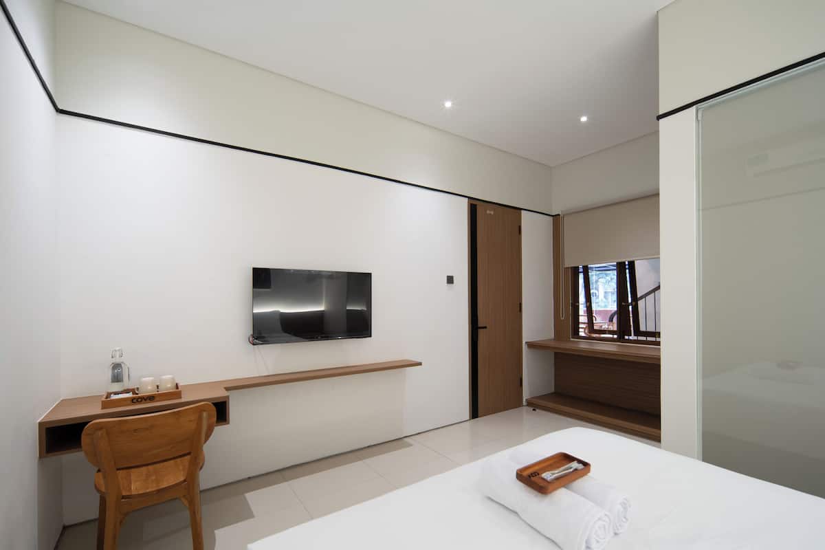 A modern hotel room with a flat-screen TV, a wooden desk, a bed with a white comforter, and a window with a view.