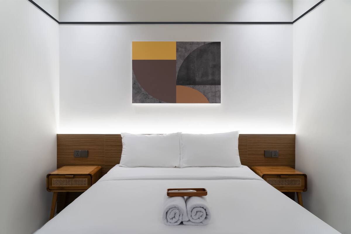 A modern hotel room with a neatly made bed, two wooden nightstands, and a wall-mounted abstract art piece.