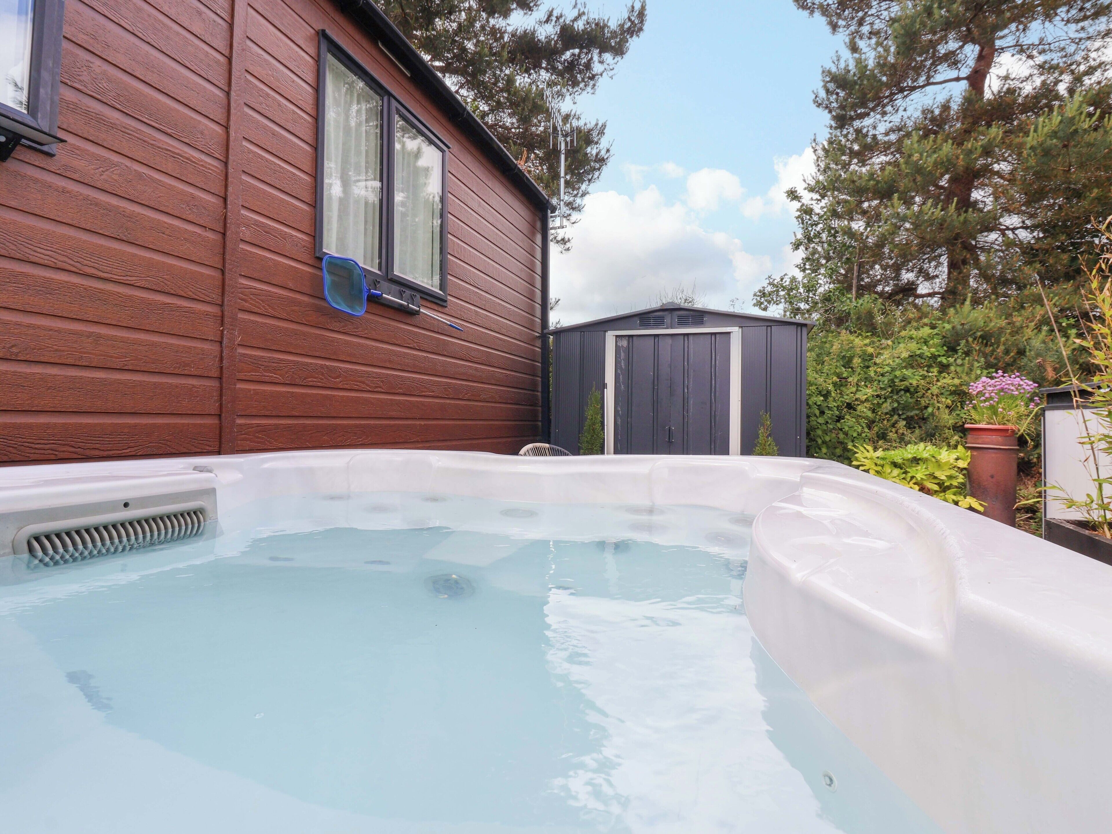 Ein Whirlpool in einem Garten mit Holzverkleidung, einem Fenster und einem Schuppen.