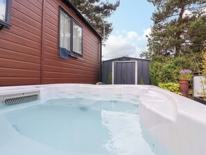 Ein Whirlpool in einem Garten mit Holzverkleidung, einem Fenster und einem Schuppen.