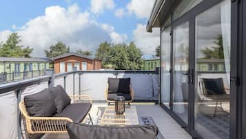 Un balcón con mobiliario de mimbre, una puerta de cristal y vistas a otros edificios.