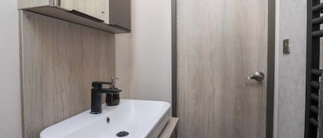 Uma casa de banho com uma pia branca, um espelho e uma porta com puxador.