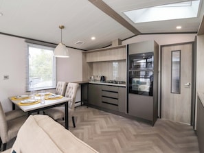 Cocina compacta con estufa a gas, horno y microondas integrado. Hay una mesa de comedor con sillas y un banco.